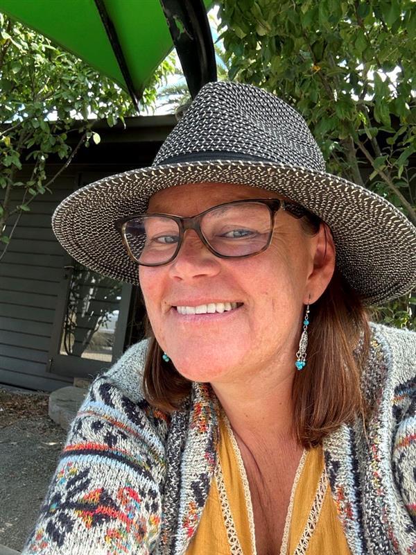 Woman wearing sunhat and glasses smiling, in garden setting